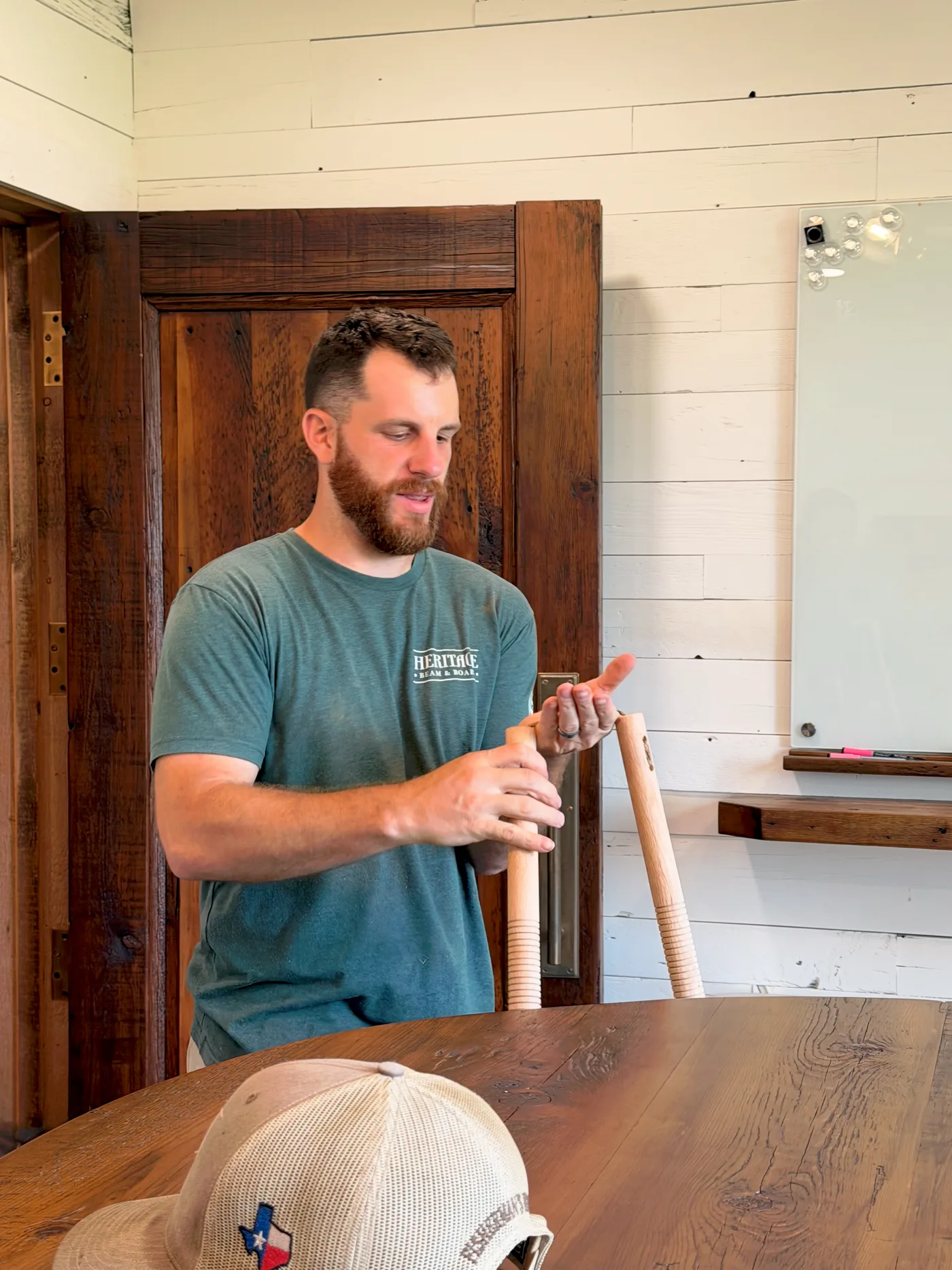 Inspecting a pair of nunchucks in the Heritage Beam & Board showroom, surrounded by reclaimed wood doors and a live-edge table