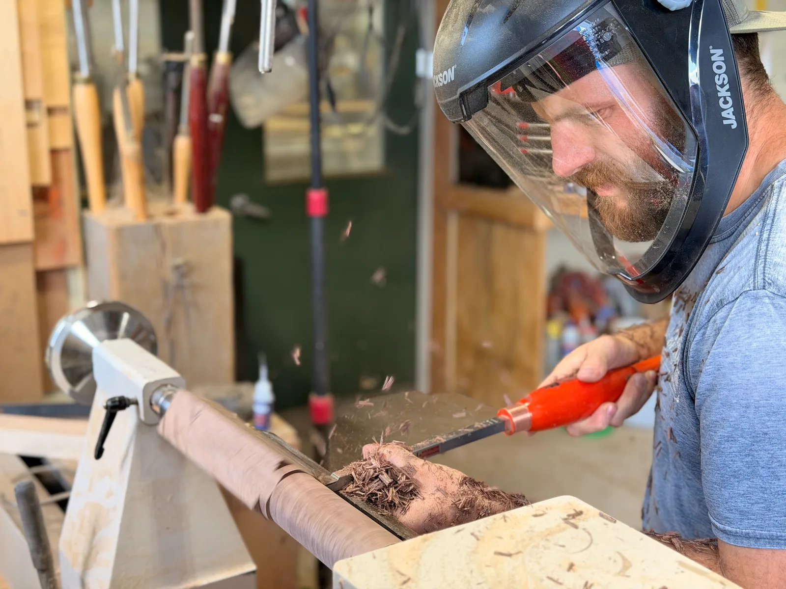 Turning a nunchuck handle on a wood lathe, shavings flying, face shield down